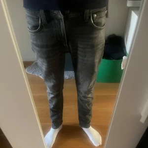 Mörk gråa Lean Dean jeans från Nudie Jeans - Säljer ett par svarta skinny jeans från Nudie Jeans med snyggt tvättad look och klassiska fem fickor. Storleken är 28 runt midjan med 30 i längd