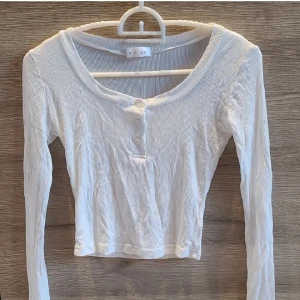 Söt vit långärmad topp med knappar - Jättesöt vit ribbad topp med lång ärm och knappar framtill. Tröjan är croppad och har en rund halsringning. Supermjukt och tunnt material. Köpt utomlands, gissar att storleken passar S, även XS. Aldrig använd