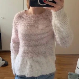 Ljusrosa fluffig stickad tröja - Supermysig stickad tröja i ljusrosa och vitt med fluffig känsla. Tröjan har rund hals och långa ärmar, perfekt för dig som gillar en chill och cozy vibe. Passar till jeans eller leggings och har en loose fit som gör den extra skön.