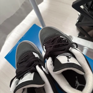Nike Air Jordan 4 svart/grå sneakers - Nike Air Jordan 4 sneakers i svart och grått med vita detaljer. Skorna har klassisk Jumpman-logga på plösen och hälen, meshpaneler på sidorna och snörning framtill. Sulan har coolt stänkmönster och ovandelen är i mocka och syntet. Perfekt för dig som gillar streetstyle.
