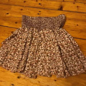 Blommig kortkjol från SHEIN - Supersöt kortkjol från SHEIN med beige botten och små vita blommor med gröna och bruna detaljer. Kjolen har en smockad midja som ger en skön och flexibel passform. Perfekt för dig som gillar romantiska och feminina vibes.