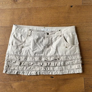 Beige volangkjol med fickor - Snygg beige kortkjol från Abercrombie & Fitch med volangdetaljer och praktiska fickor både fram och bak. Kjolen har jeansinspirerad look med bälteshällor och dekorativa sömmar. 