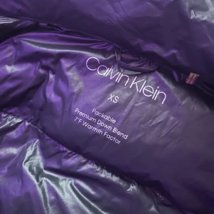 Svart dunjacka Calvin Klein XS - Snygg svart dunjacka från Calvin Klein i storlek XS. Jackan är quiltad, har dragkedja framtill och innerficka med dragkedja. Liten CK-logga på ärmen och hög krage. Säljer pga att den är för liten, (pris kan diskuteras) 