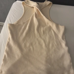 Ribbad ljus gul/beige  linnetopp från Gina Tricot - Supersnygg ribbad linnetopp från Gina Tricot i storlek S. Toppen har en twistad detalj framtill vid halsen och är ärmlös med hög halsringning. Endast använd 2 gånger. 