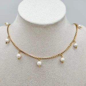 Guldhalsband med pärlor  - Unikt halsband i guldtonad kedja med hängande vita pärlor, varje pärla har en liten guldfärgad spike under sig. Kedjans tjocklek -3mm. Rostfritt stål 