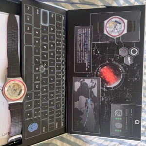 Swatch Q James Bond Special Edition - Cool Swatch Q James Bond Special Edition med transparent urtavla där du ser mekaniken. Röd och silverfärgad boett, svart och rött band med läderlook. Snygg detalj med Q-logga på urtavlan. Perfekt för dig som gillar unika accessoarer och Bond-vibbar.