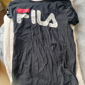 Svart FILA t-shirt med stor logga - Svart t-shirt från FILA i storlek M med stor vit och röd logga på bröstet. Klassisk rund hals och korta ärmar. Mjuk och skön bomullskvalitet som passar perfekt till jeans eller shorts. Enkel och sportig stil med loose passform.