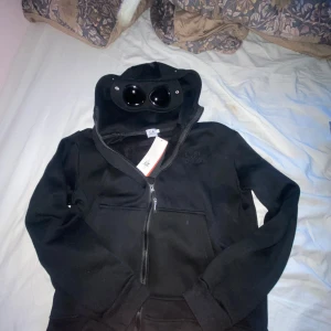 Svart hoodie från C.P. Company - Säljer en svart hoodie från C.P. Company med inbyggda glasögon i huvan. Den har en dragkedja framtill. använd fåtal gånger