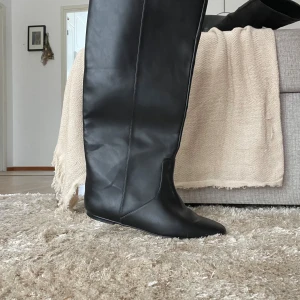 Svarta stövlar med spetsig tå - Snygga svarta stövlar i skinn med spetsig tå. Perfekta för en stilren look och passar bra till både kjol och byxor. De har en elegant design som sträcker sig upp till knäna. Perfekt för en nedhasad look