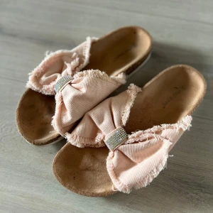 Rosa sandaler med rosett - Snygga rosa sandaler med en stor rosett och glittrande detaljer. Perfekta för sommarens varma dagar. Sandalerna har en bekväm sula och en fransig kant som ger en avslappnad look. Storlek 40 men passar nog 39 med!