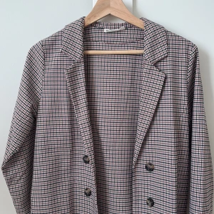 Rutig kavaj från KappAhl - Snygg rutig kavaj från KappAhl i en mix av brunt, svart och vitt. Kavajen har en klassisk krage och knäpps med knappar framtill. Perfekt för en stilren look!Köpte den ungefär för 250 och den ser ut som en helt ny kavaj. Har använt den en gång.👌🏼