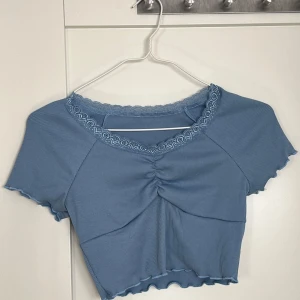 Blå ribbad topp med spetsdetaljer - Säljer en söt blå ribbad topp med spetsdetaljer runt halsen. Toppen har korta ärmar och en fin rynkning framtill. Från Shein och helt oanvänd. Är stl 158, 12-13 år. Upplevs som en small. 