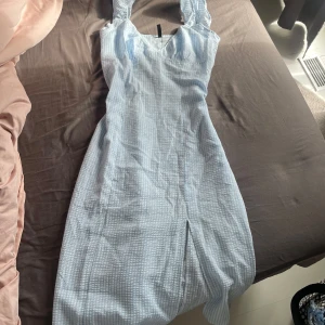 Ljusblå rutig klänning - Säljer en söt ljusblå klänning med rutigt mönster. Klänningen har breda axelband och en smickrande passform, fodralsittande med en diskret dragkedja i sidan. Perfekt för sommarevent eller skolavslutningar!