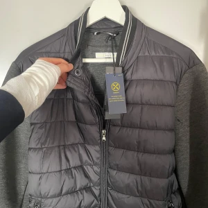 Cardigan CELIO - Snygg grå jacka perfekt för VARMA SOMMAR KVÄLLAR! med quiltad framsida och dragkedja. Ärmarna och baksidan är i ett mjukare material. Perfekt för kyligare dagar med sin stilrena design och praktiska fickor. 10/10 skick med tags! Går ner i pris vid snabb affär!!