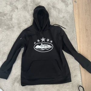 Svart corteiz hoodie - Säljer en svart hoodie med ett coolt vitt tryck på framsidan. Hoodien har en klassisk design med känguruficka och justerbar huva. Perfekt för en avslappnad stil. Hör av dig vid intresse!