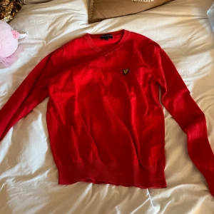 Röd tröja från Lyle & Scott - Säljer en snygg röd tröja från Lyle & Scott med deras ikoniska logga på bröstet. Tröjan har en klassisk design med ribbade muddar och rund halsringning. Perfekt för en stilren look.