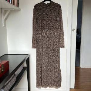 Mönstrad långklänning från Gerry Weber - Snygg långklänning från Gerry Weber med ett unikt mönster i bruna och svarta toner. Klänningen har långa ärmar och en elegant passform som passar perfekt för höst och vinter. Tillverkad i ett bekvämt material med stretch som ger en stilren look. Klänningen är fodrad förutom ärmarna. 