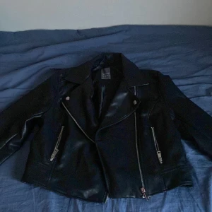 Svart skinnjacka från Primark - Snygg svart skinnjacka från Primark med dragkedjor och klassisk bikerstil. Perfekt för en cool look med sina detaljerade dragkedjor och stilrena design. Passar utmärkt till både jeans och klänning.