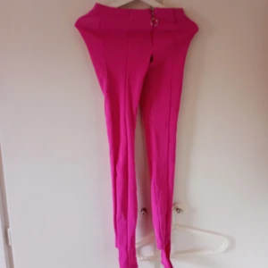 Rosa byxor med dragkedja - Snygga rosa byxor med hög midja och dragkedja framtill. Perfekta för att lägga till en färgklick i garderoben. Byxorna har en tight passform som framhäver figuren.