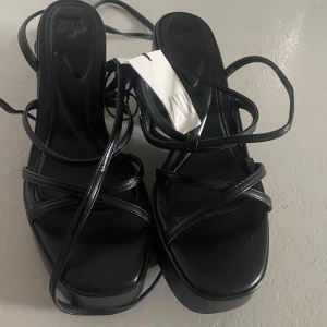 Svarta sandaler med klack från Zara - Helt nya, aldrig använd. Snygga svarta sandaler från Zara med smala remmar och klack. Perfekta för en stilren look med öppen tå och elegant design. Passar utmärkt till både vardag och fest.