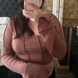 Brun ribbad topp - Säljer en snygg brun ribbad topp med långa ärmar och volangdetaljer vid ärmsluten. Toppen har en croppad passform och en fyrkantig halsringning. Perfekt för sommaren!