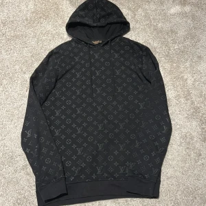Svart Louis Vuitton hoodie med monogrammönster - Snygg svart hoodie från Louis Vuitton med det ikoniska monogrammönstret. Tröjan har långa ärmar och är perfekt för en stilren och lyxig look. Den är nästan helt ny.