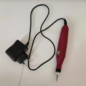 Elektrisk nagelfil - Elektrisk nagelfil i röd färg med svart sladd och laddare. Perfekt för att forma och slipa naglarna hemma. Kompakt design som är lätt att använda. 