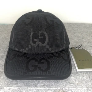 Svart gucci keps - Snygg svart keps från Gucci med det ikoniska GG-mönstret. Kepsen har en justerbar rem baktill för perfekt passform. Tillverkad i ett slitstarkt syntetmaterial som ger en lyxig känsla. Storlek ”M”