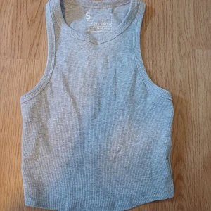 Grå ribbad linnetopp från FSBN Sister - Säljer en stilren grå ribbad linnetopp från FSBN Sister. Perfekt för varma dagar eller som lager under en jacka. Toppen har en enkel och klassisk design med ärmlös skärning. Säljer för att jag inte använder den. Har använt den 2 eller 3 gånger innan. Storlek S
