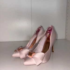 Rosa pumps med rosett - Eleganta rosa pumps med en söt rosett framtill och en stilren klack. Perfekta för att ge en feminin touch till din outfit.