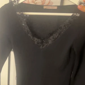 Svart tröja från Anna Field - Snygg svart tröja från Anna Field med spetsdetaljer vid halsringningen. Tröjan har en v-ringad design och långa ärmar, perfekt för en stilren look. Storlek xs men är väldigt stretchig i materialet 