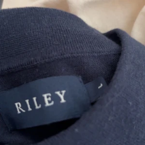 Mörkblå t-shirt från Riley - Säljer en stilren mörkblå t-shirt från Riley med vita detaljer vid ärmslut och krage. Perfekt för en avslappnad look. T-shirten har korta ärmar och en klassisk passform.