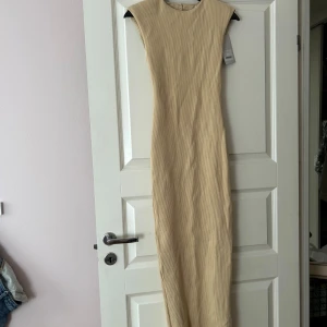 Beige långklänning från AVORA - Snygg beige långklänning från AVORA med en elegant öppen rygg och rund halsringning. Klänningen har en figurnära passform och är perfekt för en stilren look. Mjuk och stretchig.