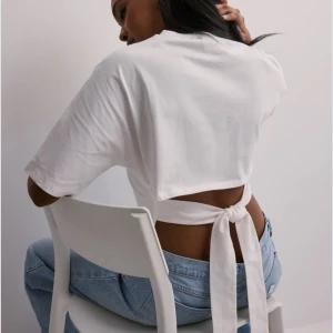 Vit kortärmad topp med knyt från Nelly - Säljer en stilren vit topp med korta ärmar och knytning i ryggen. Perfekt för en avslappnad look med en knut i ryggen. 