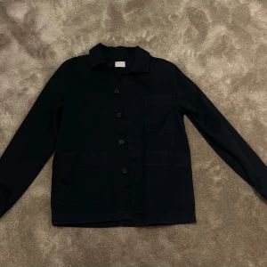 Mörkblå overshirt med knappar - Snygg mörkblå overshirt med knappar framtill och klassisk krage. Perfekt för lager-på-lager-stil. Har två stora fickor framtill för extra funktionalitet.