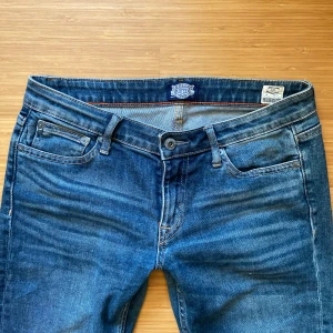 Blå jeans från - Snygga blå jeans med klassisk femficksdesign och knappgylf. Perfekta för en avslappnad stil. De har en lätt tvättad look som ger en cool vintagekänsla.