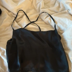 Svart linne med smala axelband - Säljer ett stilrent svart linne med smala axelband och elastisk rygg för en bekväm passform. Perfekt för varma dagar eller som lager under en kavaj. Passar till många olika stilar och tillfällen.