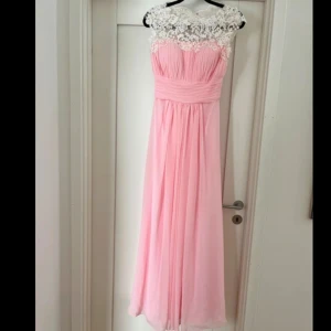 Rosa långklänning med spetsdetaljer - Rosa långklänning med vacker spets upptill och plisserad midja. Perfekt till bal eller andra tillställningar. Aldrig använd bara testad 