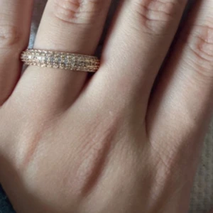 Glittrig ring i guld - Säljer en elegant glittrig ring i guldton med flera rader av små gnistrande stenar. Perfekt för att ge en touch av glamour till vilken outfit som helst. Passar utmärkt för speciella tillfällen.