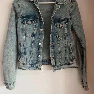 Blå jeansjacka - Snygg blå jeansjacka med klassisk design och knappar framtill. Jackan har två bröstfickor med lock och knappar samt två sidofickor. Perfekt för en avslappnad stil.