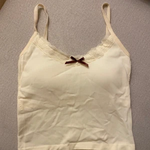 Coquette linnetopp med spetsdetaljer - Söt beige linnetopp med smala axelband och spetsdetaljer vid halsringningen. Perfekt för varma dagar eller som ett lager under andra plagg. Köpte i Japan ❤️