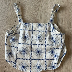 Vit och blå broderad linnetopp från Zara - Charmig vit linnetopp från Zara med blått blommönster och broderade detaljer. Toppen har smala axelband och en luftig passform, perfekt för varma dagar. Ett stilrent val för en somrig look! 🌼
