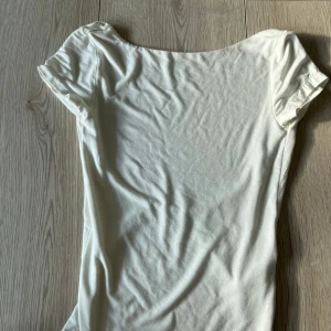 Vit topp från Gina Tricot - Säljer en stilren vit topp från Gina Tricot i storlek XS. Toppen har korta ärmar och en djup öppen rygg som ger en elegant touch. Perfekt för varma dagar eller som ett basplagg i garderoben.🩷🩷
