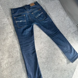 Nudie jeans - Riktigt snygga mörkblå nudie jeans i modellen thin finn! Storlek W33 L32, passar dock mindre än så. Väldigt bra skick, endast förstärkta mellan benen. Skriv om ni har några frågor!