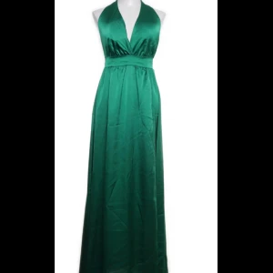 Grön halterneck långklänning i satin - Snygg grön långklänning i satin med halterneck och djup v-ringning. Klänningen har markerad midja och knyts i nacken för en elegant siluett. Perfekt för speciella tillfällen. Köpt second hand superbra skick använd en gång under balen. 