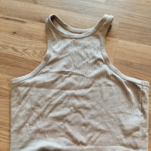 Beige ribbad linnetopp från H&M Divided - Säljer en beige ribbad linnetopp från H&M Divided. Toppen har en tight passform och är ärmlös med rundad halsringning. Perfekt för varma dagar eller som lager under andra plagg.