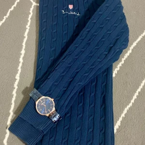 Mörkblå stickad tröja från Bondelid - Säljer en mörkblå kabelstickad tröja från Bondelid med rund halsringning och broderad logga på bröstet. Tröjan har långa ärmar och ribbade muddar vid ärmslut och nederkant. Perfekt för kyligare dagar.