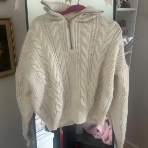 Vit kabelstickad tröja med half zip - Säljer en krämvit kabelstickad tröja med hög krage och halv dragkedja. Tröjan har långa ärmar, breda muddar och oversized passform. Perfekt för lager-på-lager och riktigt mysig till kyliga dagar. Knappt använd. Från BDG Urban Outfitters.