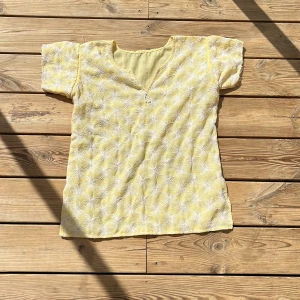 Gul blommig blus - Söt gul blus med vita blommor och v-ringning. Kortärmad och i ett lätt, luftigt tyg som passar perfekt nu till sommaren. Passar Xs/S