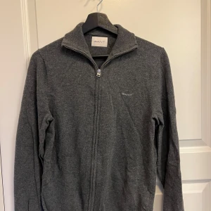 Mörkgrå ziptröja från GANT - Säljer en mörkgrå ziptröja från GANT med hög krage och dragkedja hela vägen. Grymt snygg, mycket sparsamt använd utan tydliga spår av användning. Uppskattningsvis använt den 5 gånger. Nypris 1700. Storlek S, köpt från Zalando. Jätte fint material och grym passform, perfekt att ha över en skjorta eller bara en vanlig tshirt. Hör av er vid minsta fundering👍